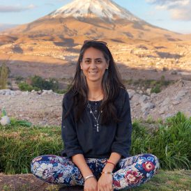 Woman sitting cross-legged looking happy and confident on rock, in front of a mountain at sunset