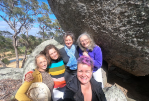 Five women seated on a boulder in an Australian bush hillside